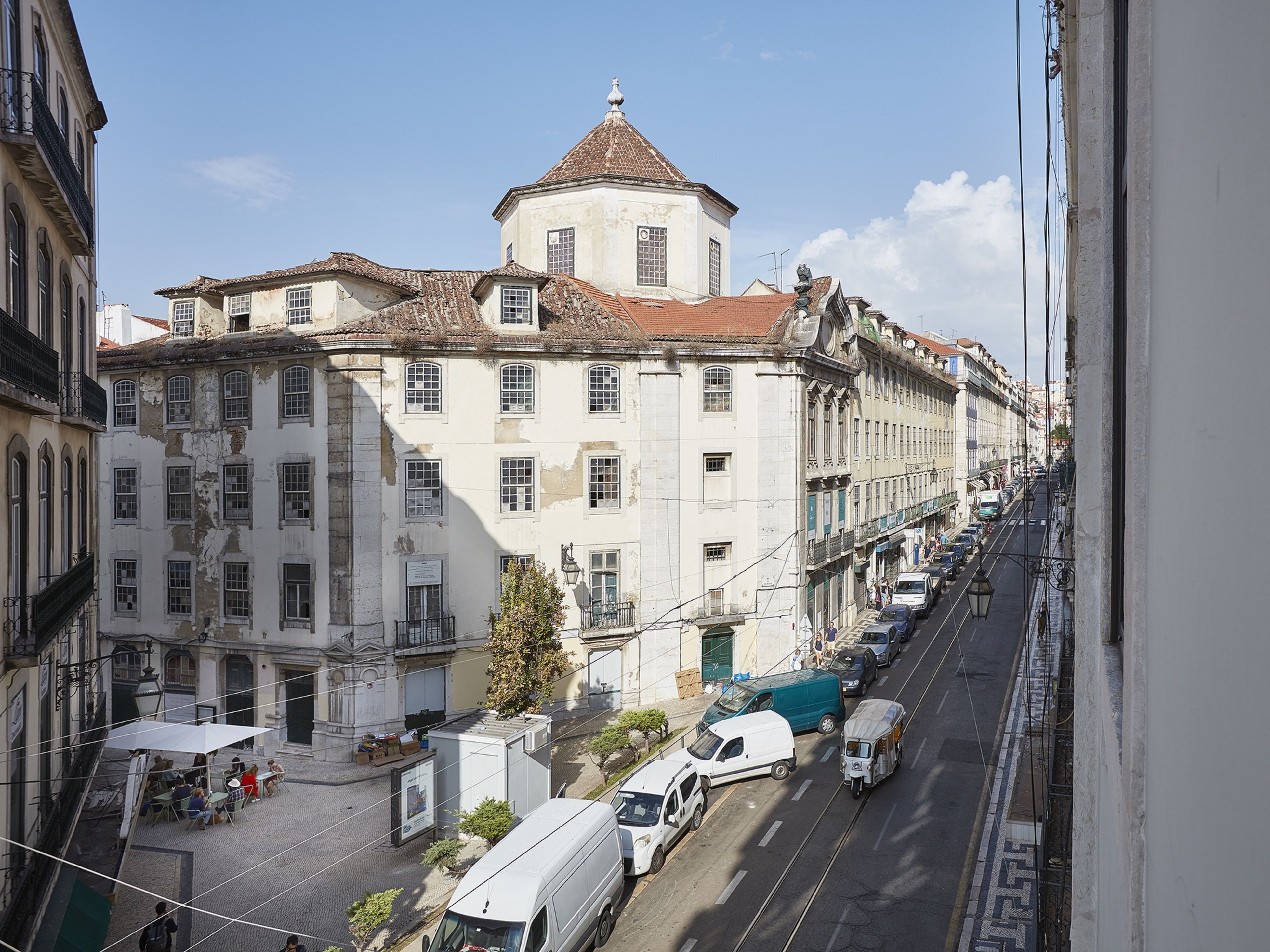 A street view with buildings, a tram, and parked vehicles.