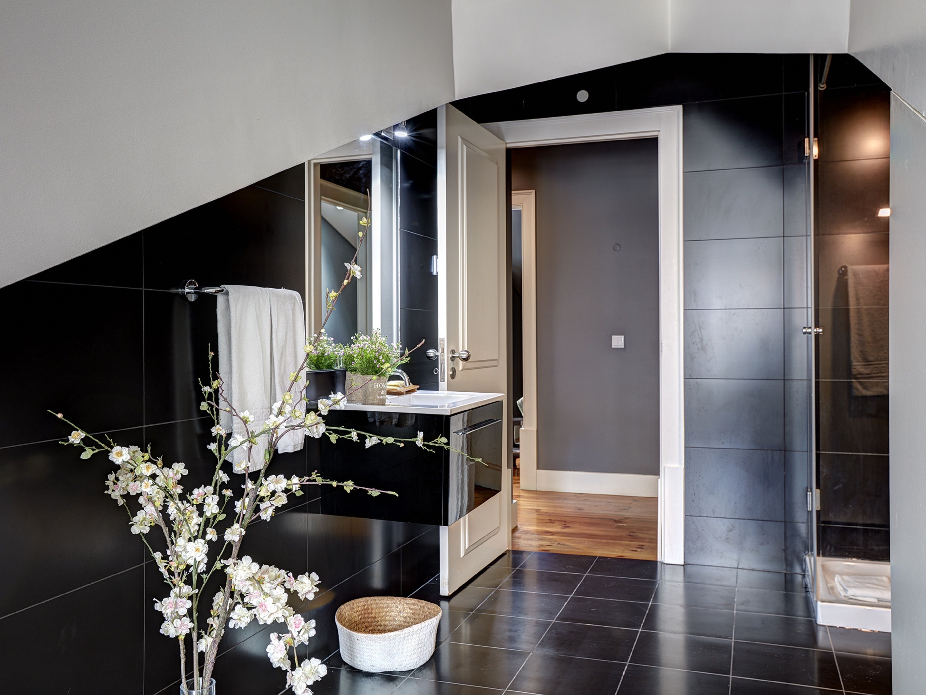 A modern bathroom with a black tiled floor, a white sink, a mirror, and a white towel hanging on the wall.