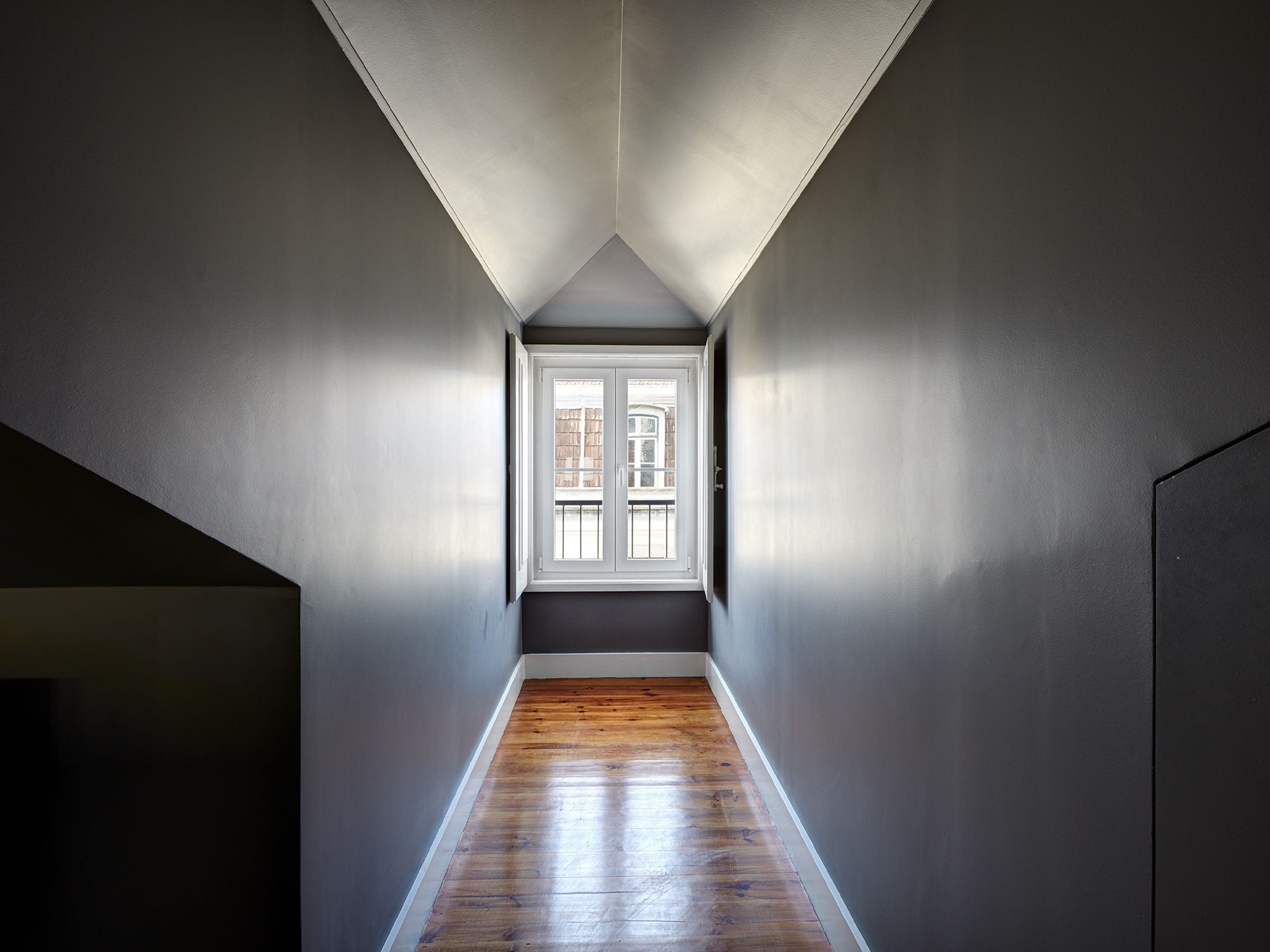 A narrow hallway with wooden flooring and a skylight at the end.