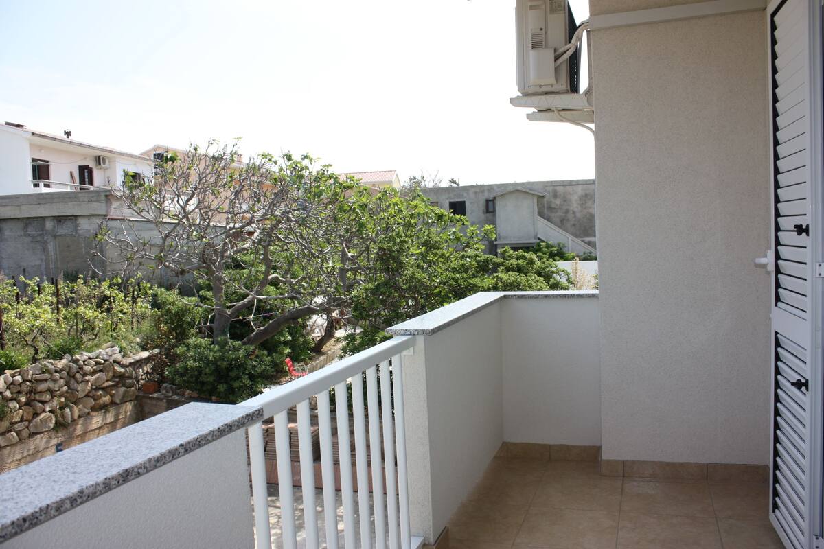 Un balcon avec un mur en pierre, un arbre et une vue sur les bâtiments voisins.