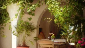 An outdoor patio with a wooden table and chairs, surrounded by potted plants and flowers. - Hotel Arisha (Houmt Souk)