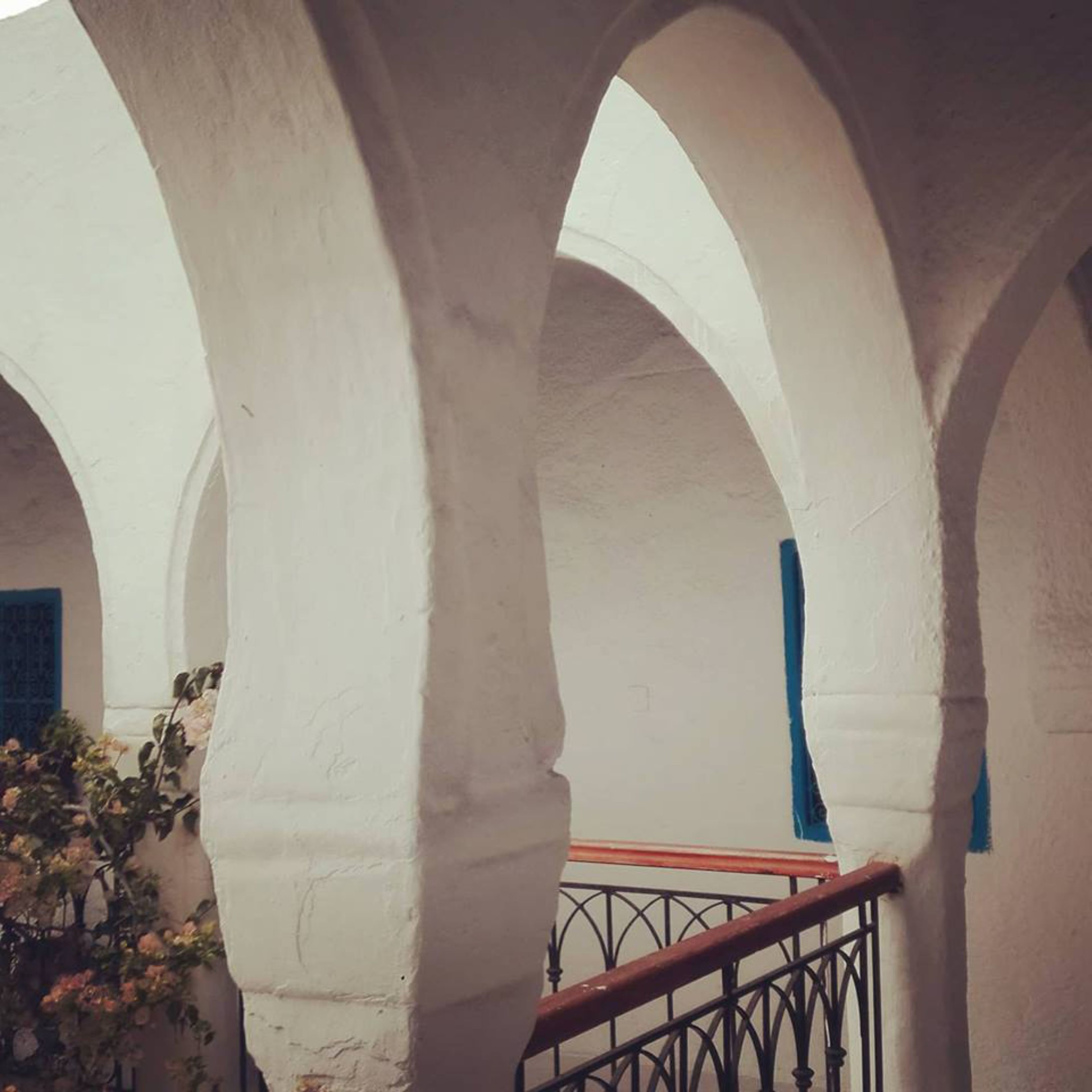 Une structure architecturale aux murs blancs et aux arches, un escalier doté d’une rampe en métal et un rideau bleu.