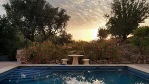 A swimming pool with a stone wall and a table with chairs in the background. - La Fuente Retreat (Lecrin)