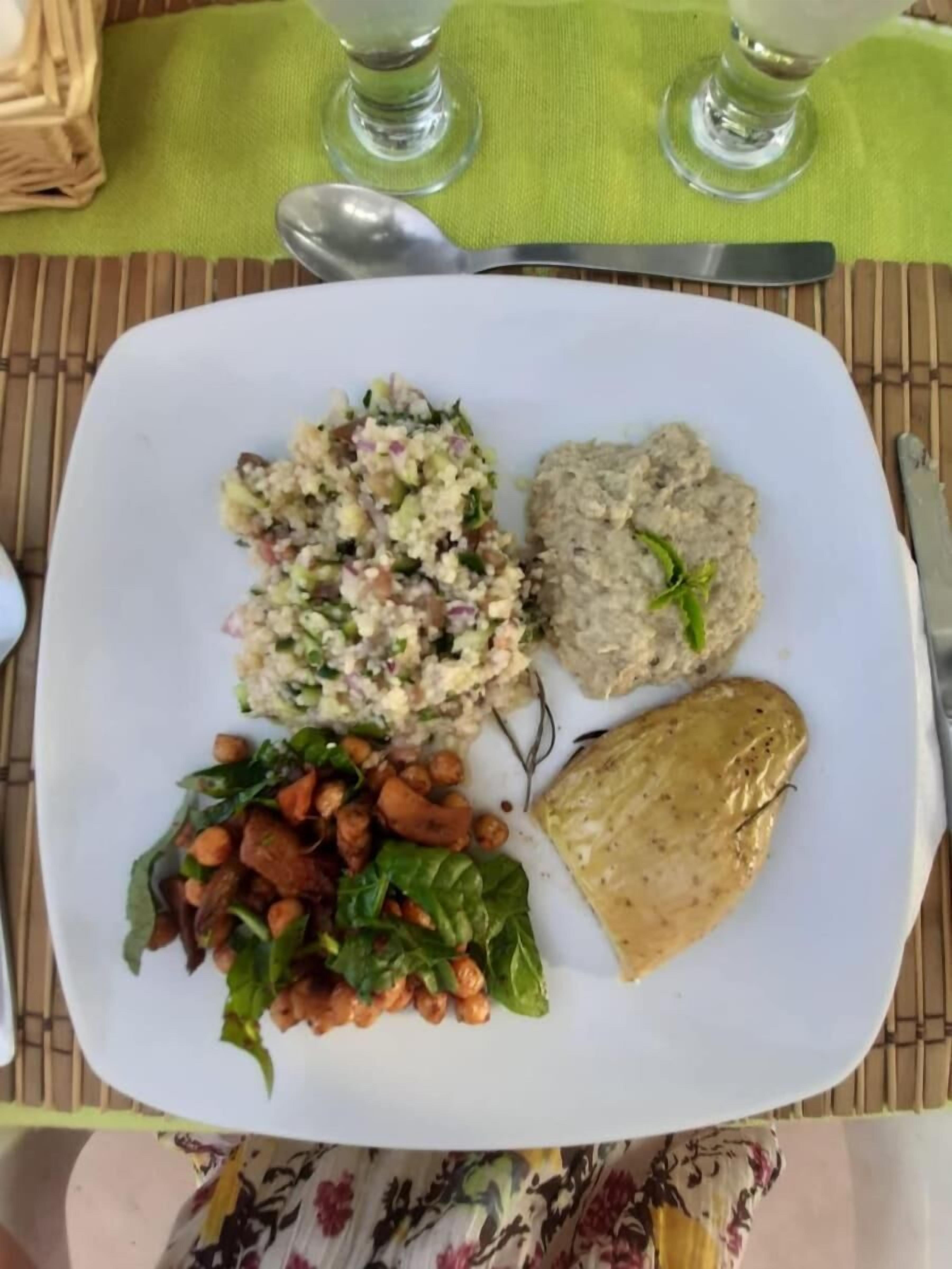 Une assiette contenant une salade, du houmous, des pois chiches et du pain pita.