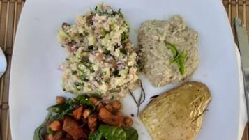 Une assiette contenant une salade, du houmous, des pois chiches et du pain pita.