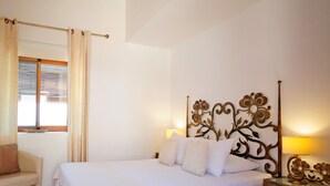 A bedroom with a bed, a chair, a bedside table, and a window with curtains. - La Fuente Retreat (Lecrin)