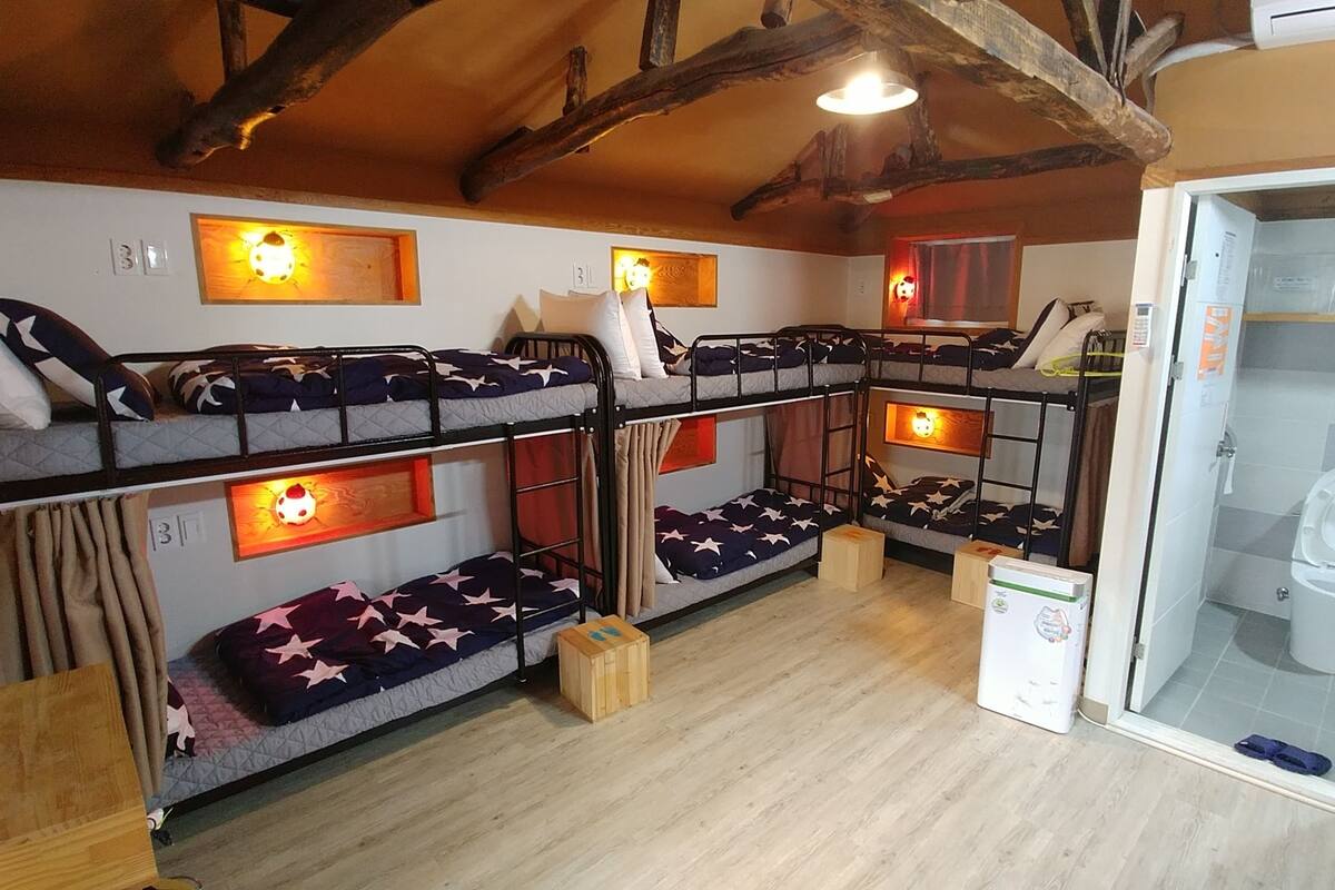 Une chambre avec un lit superposé, dotée de draps à motifs d’étoiles, de têtes de lit en bois et d’un petit réfrigérateur.