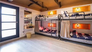 Habitación tipo dormitorio con literas, techo de madera, ventana y un cesto de basura pequeño.