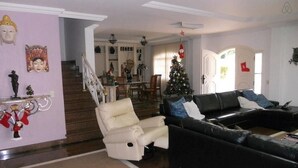 A living room with a white armchair, black leather sofa, and a Christmas tree. - Alameda dos Eucalipitos (Rio de Janeiro)