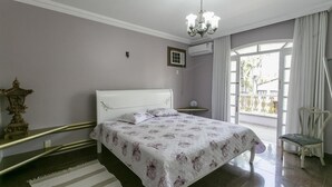A bedroom with a bed, a chandelier, a chair, and a view through a door. - Alameda dos Eucalipitos (Rio de Janeiro)