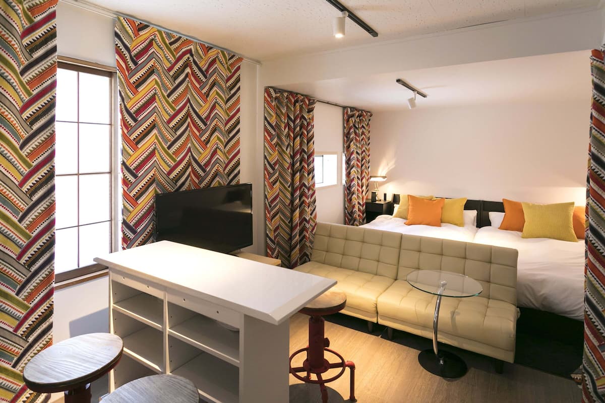 Habitación de hotel con sofá cama, una mesita, televisor y escritorio con estanterías.