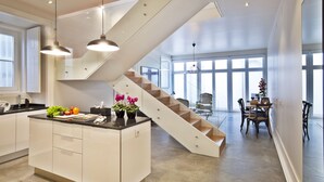 A modern kitchen with a central island, a staircase, and a dining area with natural light.