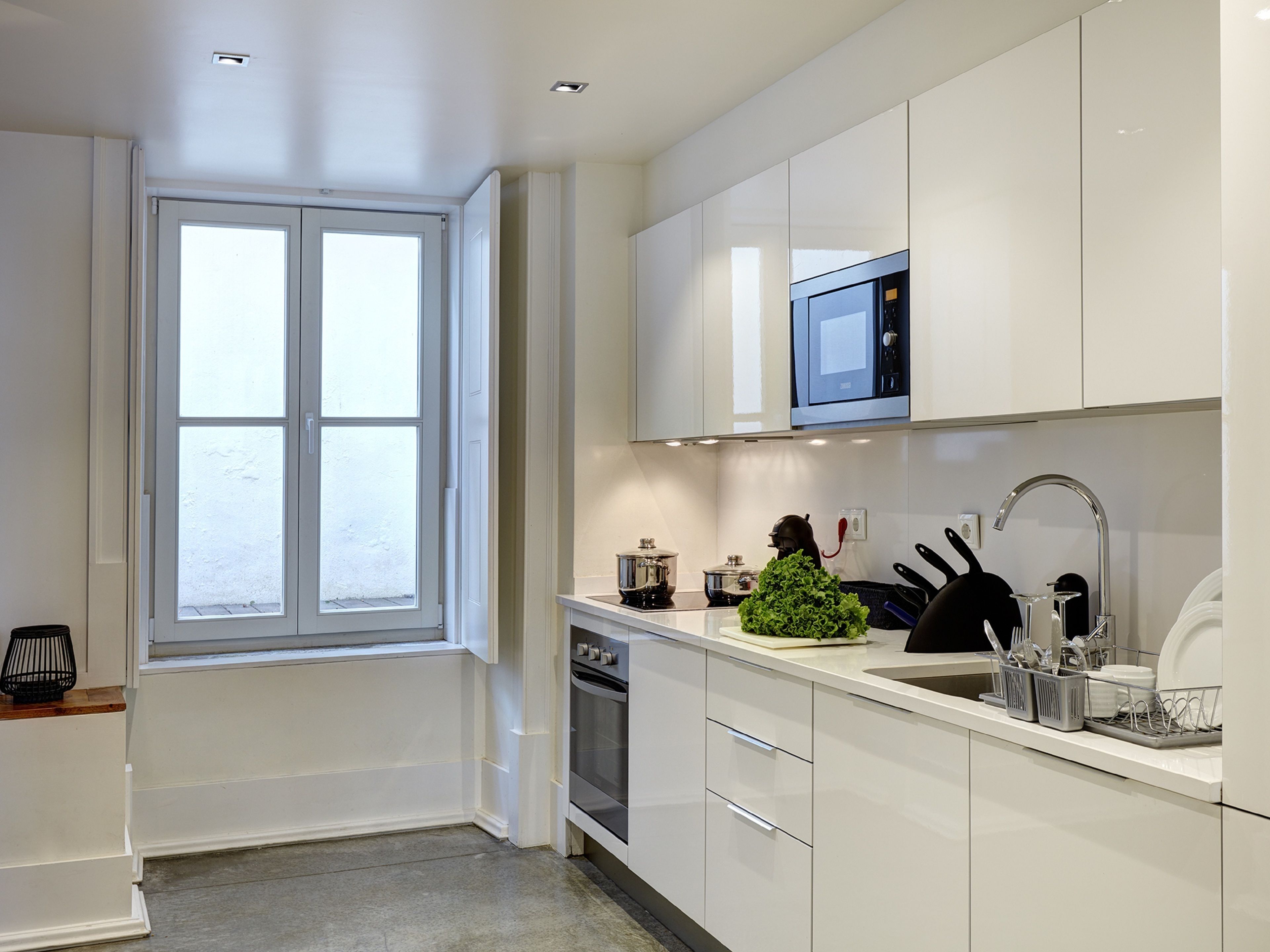 A modern kitchen with white cabinetry, a built-in microwave, and a window with a view.