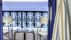 Ein Balkon mit Blick auf das Meer, zwei Stühle, ein kleiner Tisch und ein Vorhang.