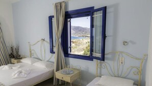 Ein Zimmer mit zwei Betten, einem kleinen Tisch und einem Fenster mit Vorhängen.