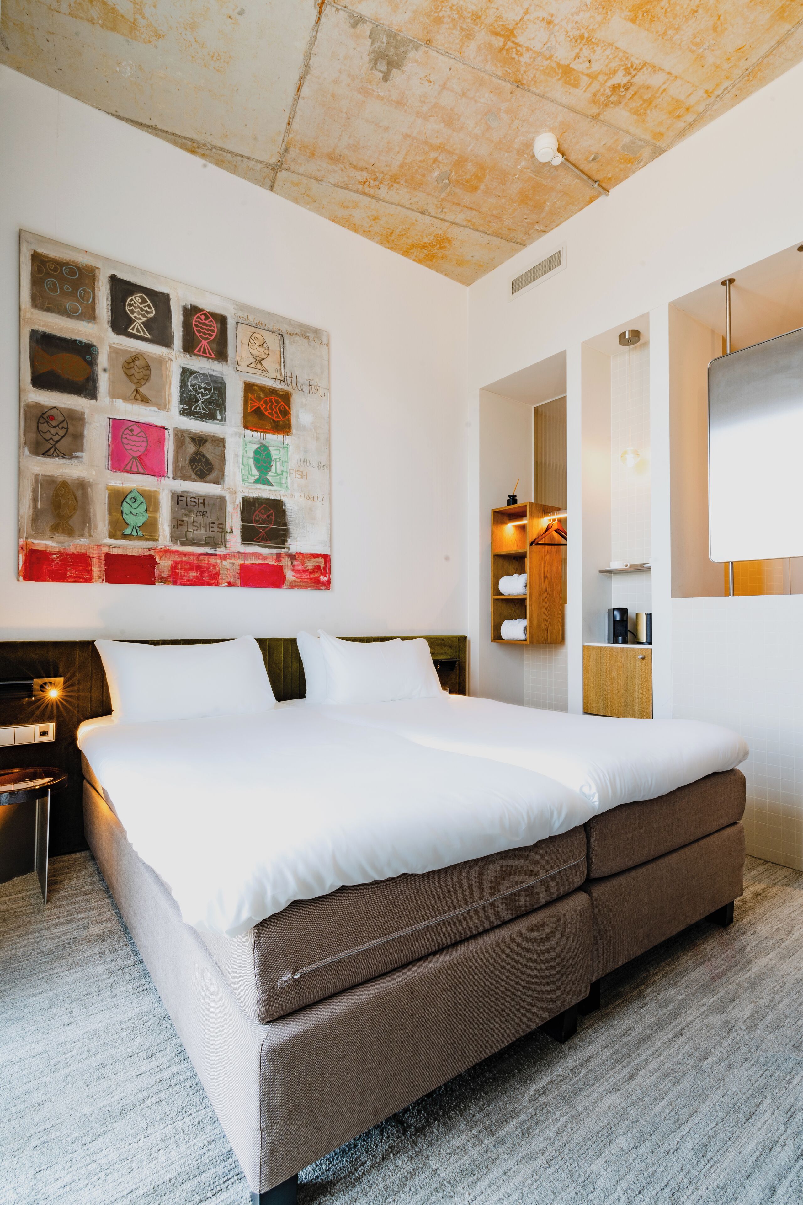 Een moderne hotelkamer met een groot bed, een kunstwerk aan de muur, een houten garderobe en een spiegel.
