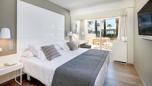 A modern hotel room with a large bed, a desk, and a balcony with a view of palm trees and a pool. - Protur Bonamar Hotel - Adults Only (Son Servera)