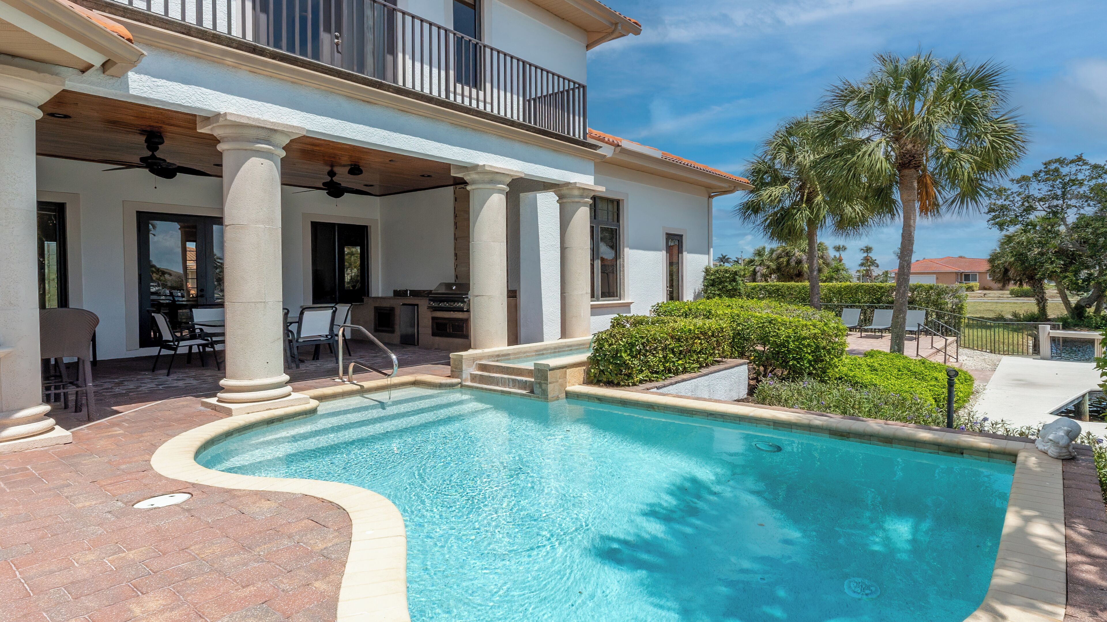 A pool area with a curved design, outdoor seating, and a covered patio with columns.