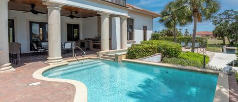 A pool area with a curved design, outdoor seating, and a covered patio with columns.