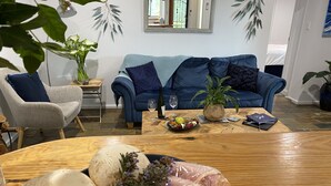 A living room with a blue sofa, a wooden coffee table with food, a chair, and a plant.