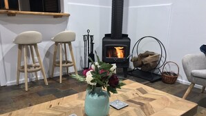 A cozy living room with a wooden coffee table, a vase with flowers, a fireplace, and a window with a view.