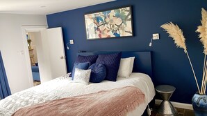 A bedroom with a bed, a painting, and a vase with pampas grass.