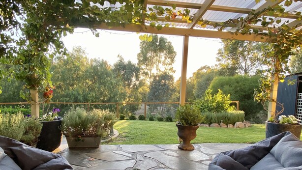 A covered patio with outdoor furniture, potted plants, and a view of a well-maintained garden.