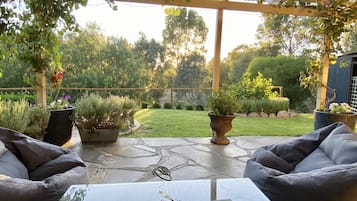 Relax in a serene garden setting with a covered patio featuring cushioned seating areas and lush greenery.