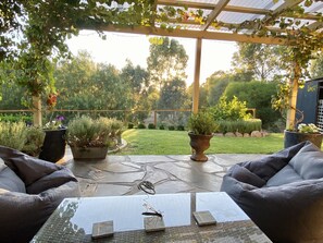 Un patio couvert, aménagé avec du mobilier d’extérieur, des plantes en pot et offrant une vue sur un jardin bien entretenu.