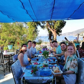 A group of people dining outdoors at a table with a view of the sea. - Turkuaz Pansiyon (Kas)