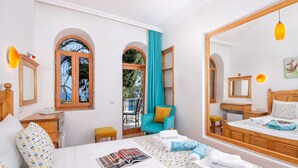 A hotel room with a bed, a desk, a chair, a mirror, and a view of the outside. - Turkuaz Pansiyon (Kas)
