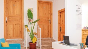 A reception area with wooden doors, a staircase, a potted plant, a blue sofa, and a desk with a laptop. - Turkuaz Pansiyon (Kas)