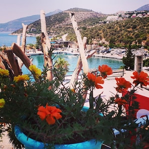 A coastal view with a pool area, wooden structures, and a mountainous backdrop. - Turkuaz Pansiyon (Kas)