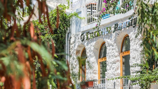 A building with a stone facade, arched windows, and a balcony with potted plants. - Turkuaz Pansiyon (Kas)