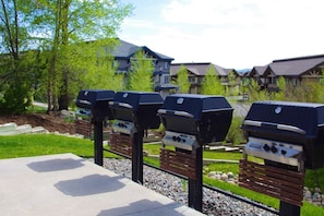 Outdoor barbecue grills, a concrete bench, and a grassy area with a pathway. - Great Value Close to Resort w/Heated Pool-Hot Tubs-Grills-Looping Ski Shuttle-Gas Fireplace-Updated (Steamboat Springs)