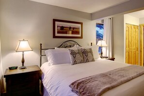 A neatly made bed with white linens and patterned pillows, a bedside table with a lamp, and a framed picture on the wall. - Long Weekend Savings! Stay Longer for Labor Day for Less! (Steamboat Springs)