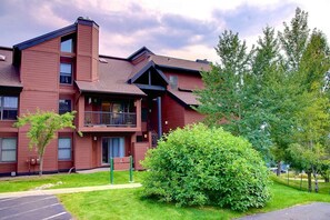 A multi-story building with a red exterior, a balcony on the second floor, and a well-maintained lawn with a large bush.