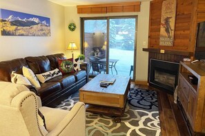 A living room with a fireplace, a sofa, a coffee table, and a view of a snowy outdoor area.