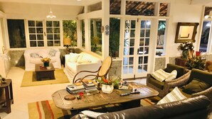 Un salon comprenant un canapé, un fauteuil et une table basse, une cheminée, et une vue dégagée grâce à de grandes portes vitrées.