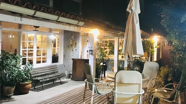 Un espace extérieur aménagé en terrasse, avec un sol en bois, des chaises blanches, un banc et des plantes en pot.