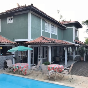 A two-story house with a swimming pool, outdoor seating area with tables and chairs, and a covered patio.