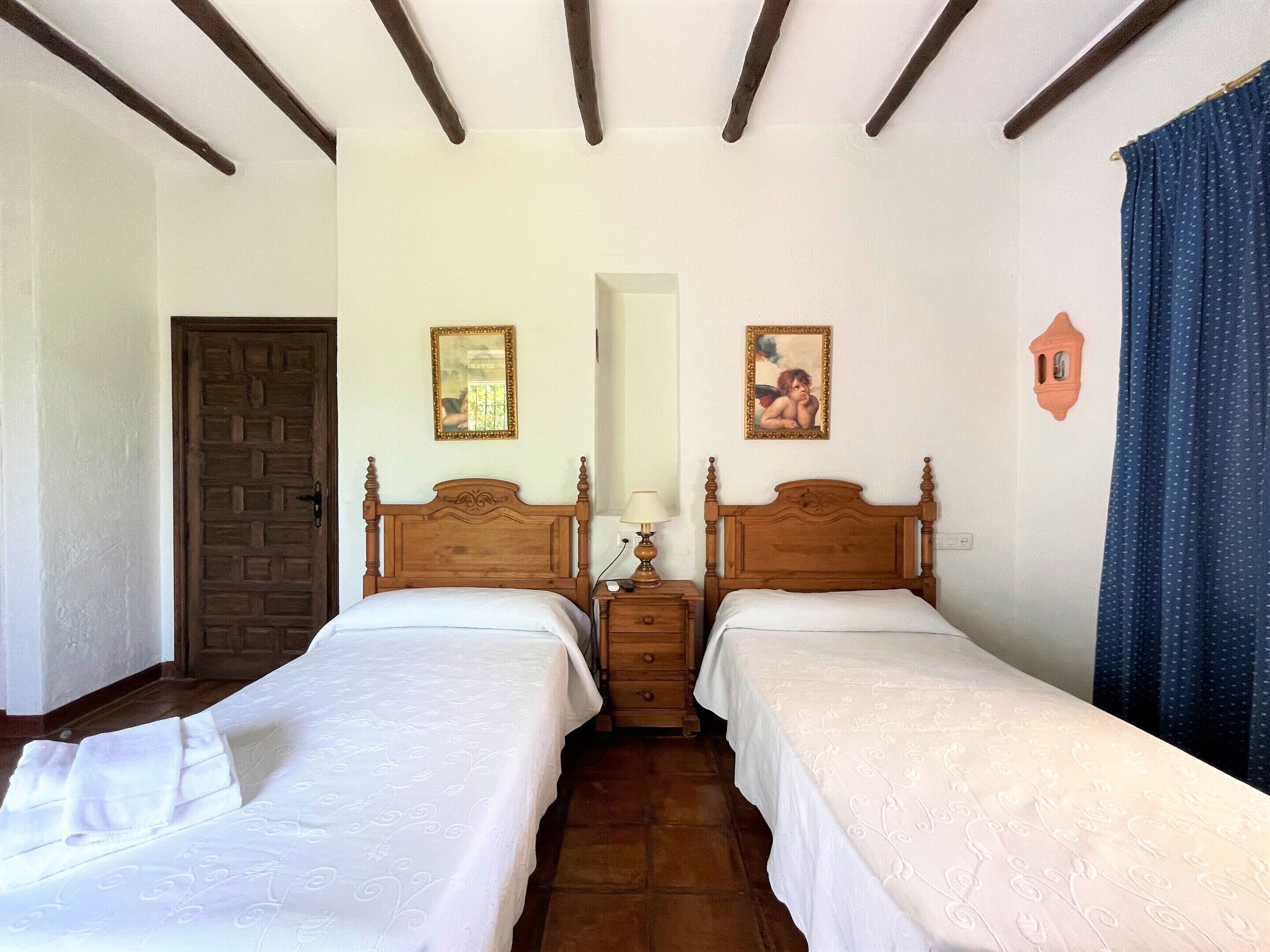 A bedroom with two wooden beds, a nightstand with a lamp, a mirror, and a wall clock.