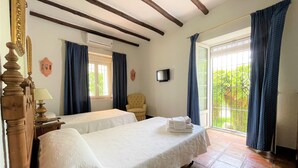Un dormitorio con dos camas, una silla, un televisor y un balcón con cortinas.