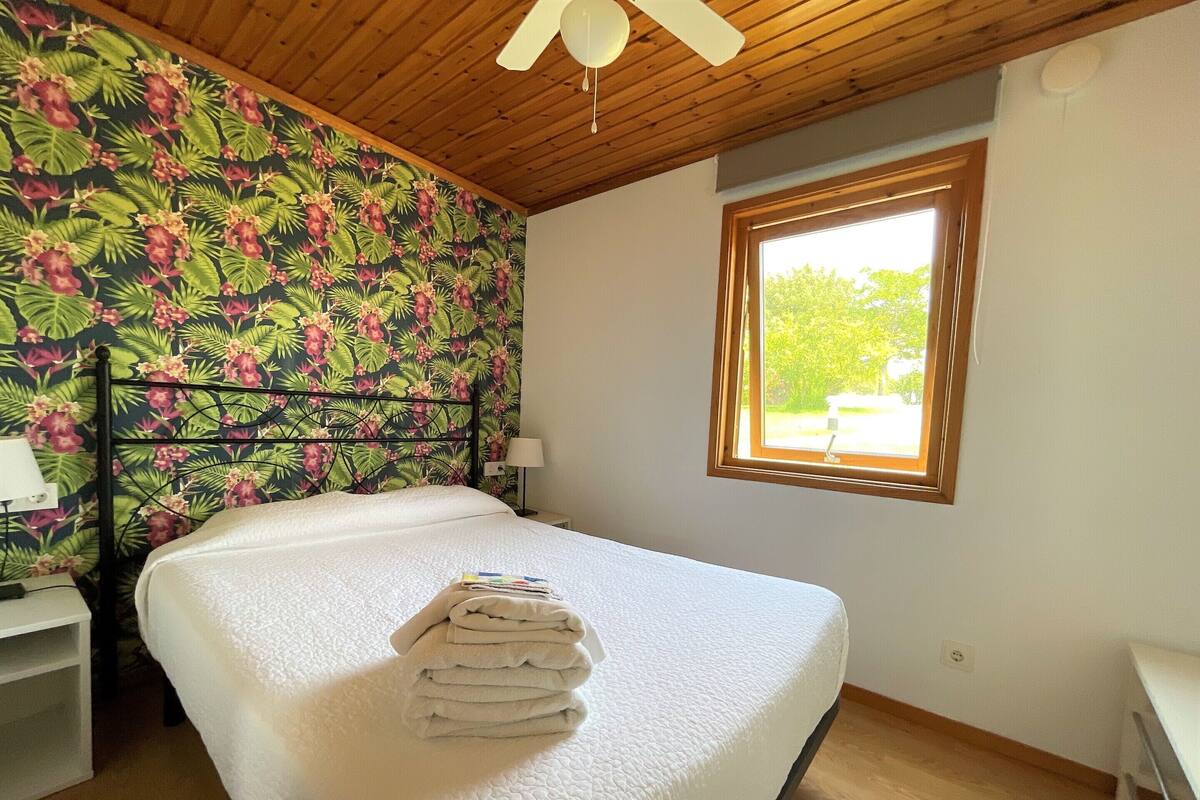 Une chambre à coucher avec un lit, une fenêtre, un ventilateur de plafond et une table de chevet.