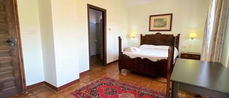 Un dormitorio con cama de madera, dos lámparas de noche, un tapete rojo estampado y un banco de madera.