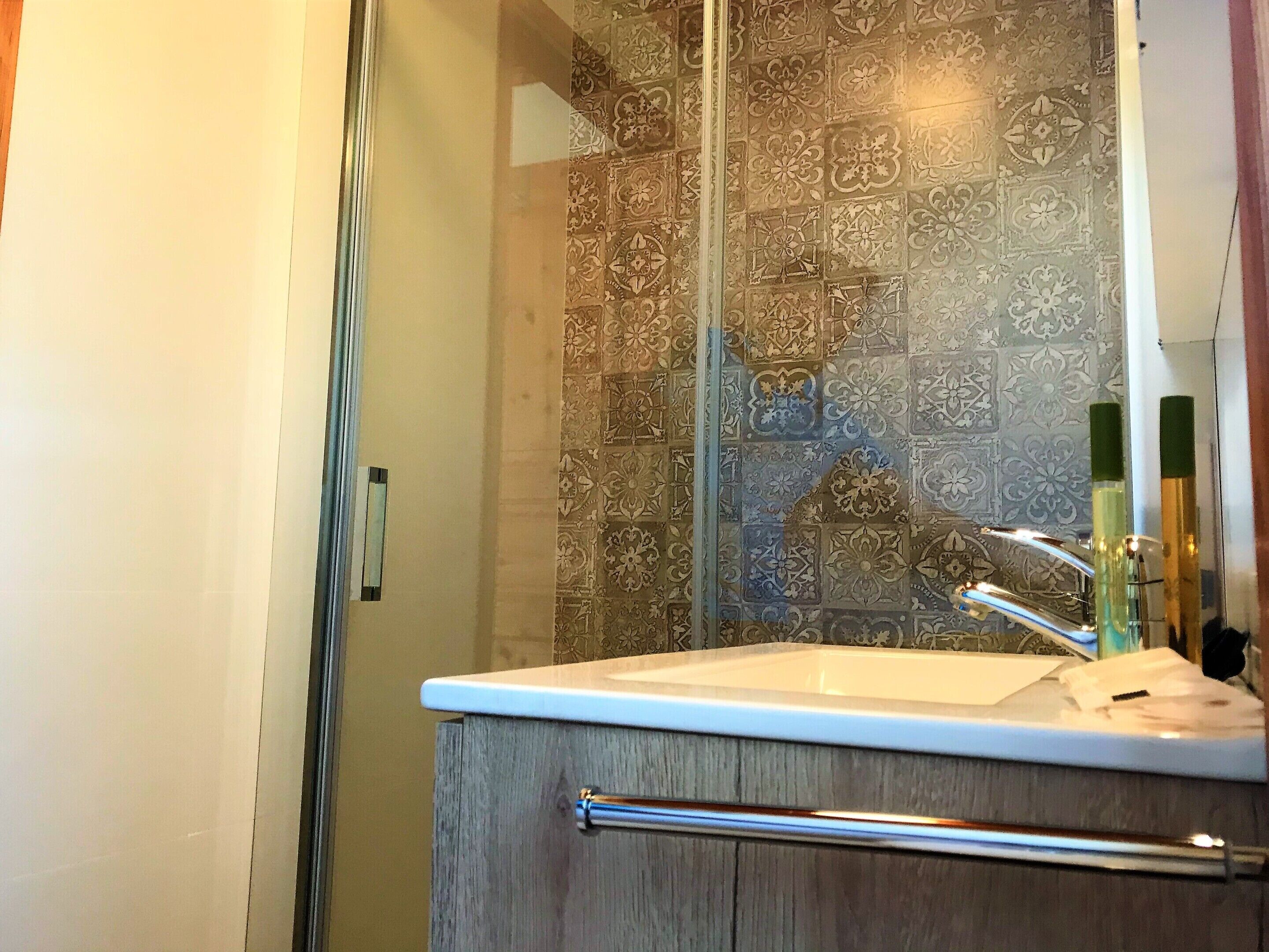 Un baño con cabina de ducha de cristal, un lavabo blanco y una pared decorada con azulejos.
