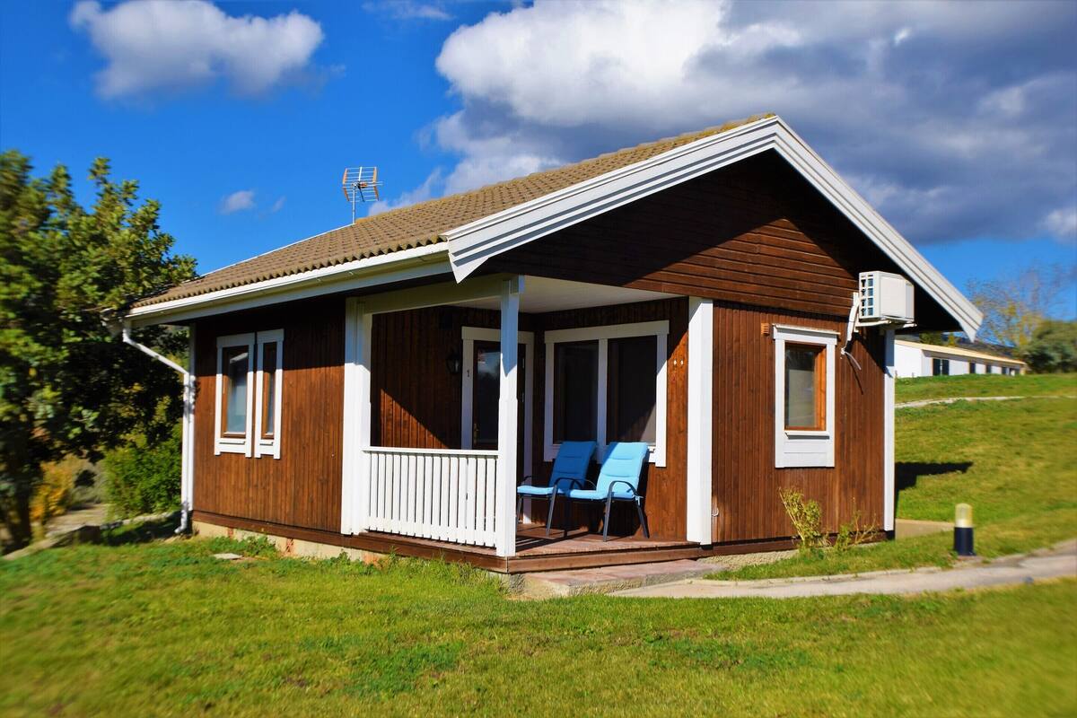 Une maison en bois d’un seul étage, dotée d’un porche, de deux fenêtres et d’un petit garage attenant.