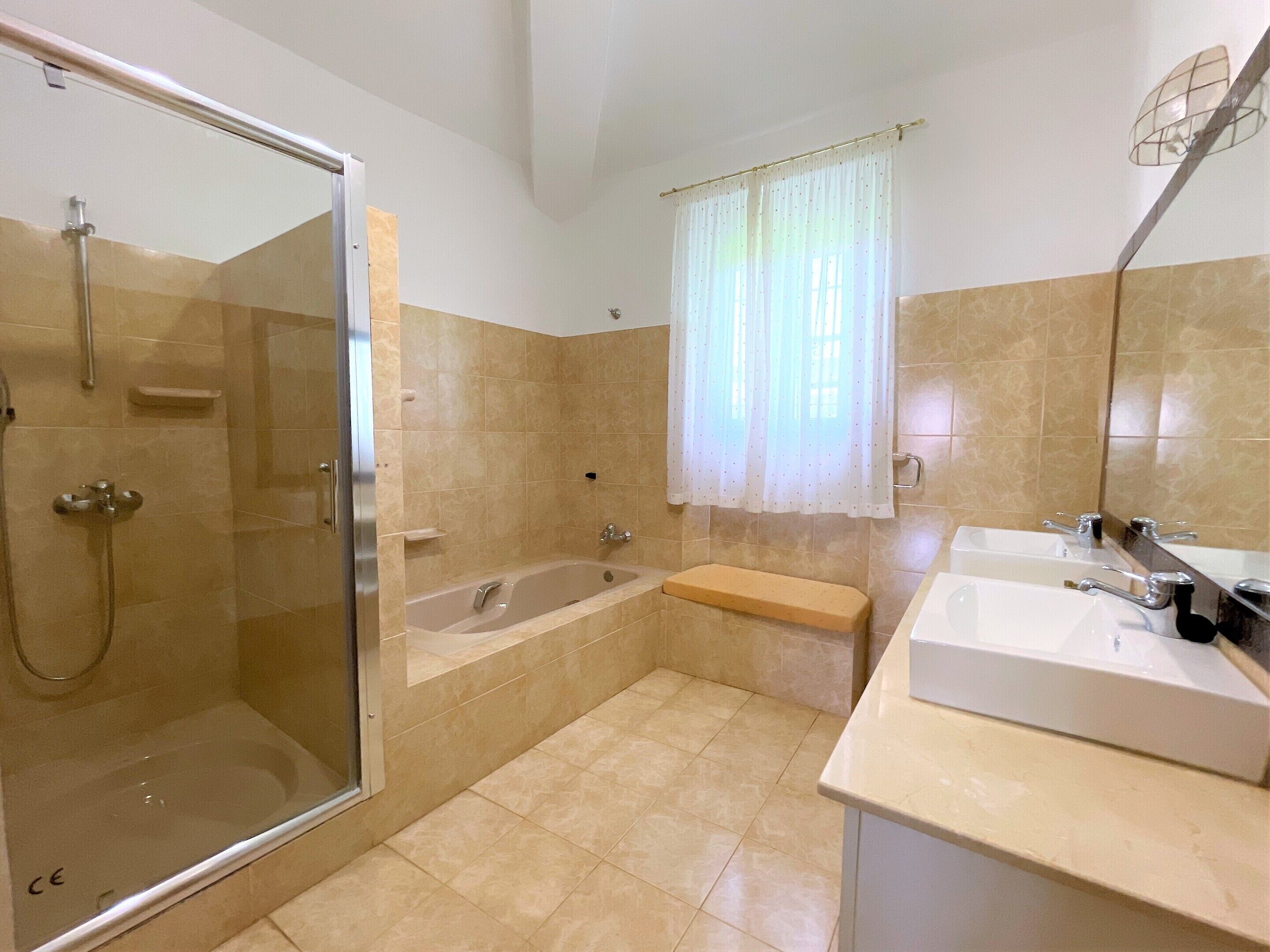 Een badkamer met een glazen douchecabine, een bad en een wastafel met spiegel.