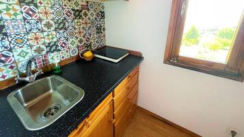 A kitchen with a black countertop, stainless steel sink, wooden cabinets, and a colorful tile backsplash.