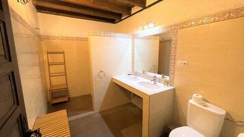 A bathroom with a wooden bench, a double sink vanity, a toilet, and a mirror with lights.